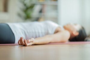 A woman lying on a yoga mat with hands relaxed out to the side.