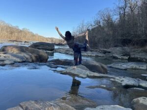 Photo of Haley Bonilla doing a yoga pose while standing on a bolder in a creek.