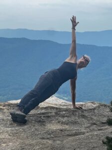 Photo of Suzanna Hasnay in a plank pose on top of a mountain. 
